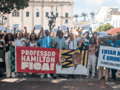 Foto de diversas pessoas segurando faixas com os dizeres: "Professor Hamilton Fica!" e "Lutar não é crime! Estamos com o professor Hamilton!"